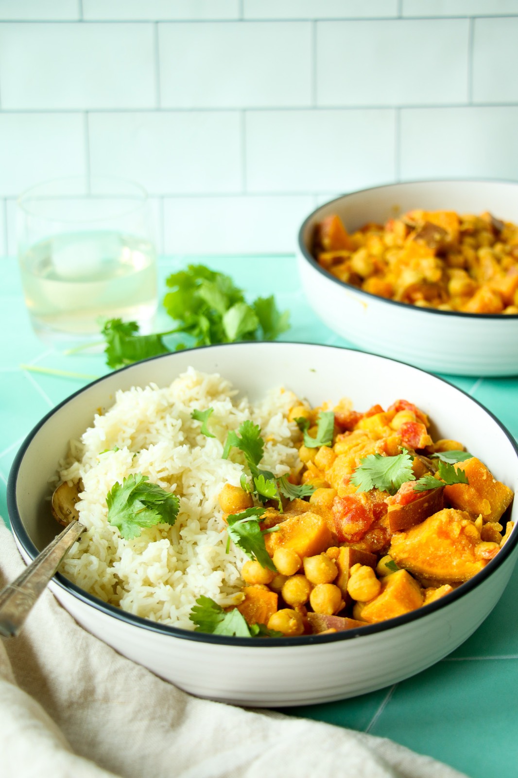Chickpea sweet potato curry without coconut milk in a white bowl on a green tiled background, shot at a 45 degree angle.