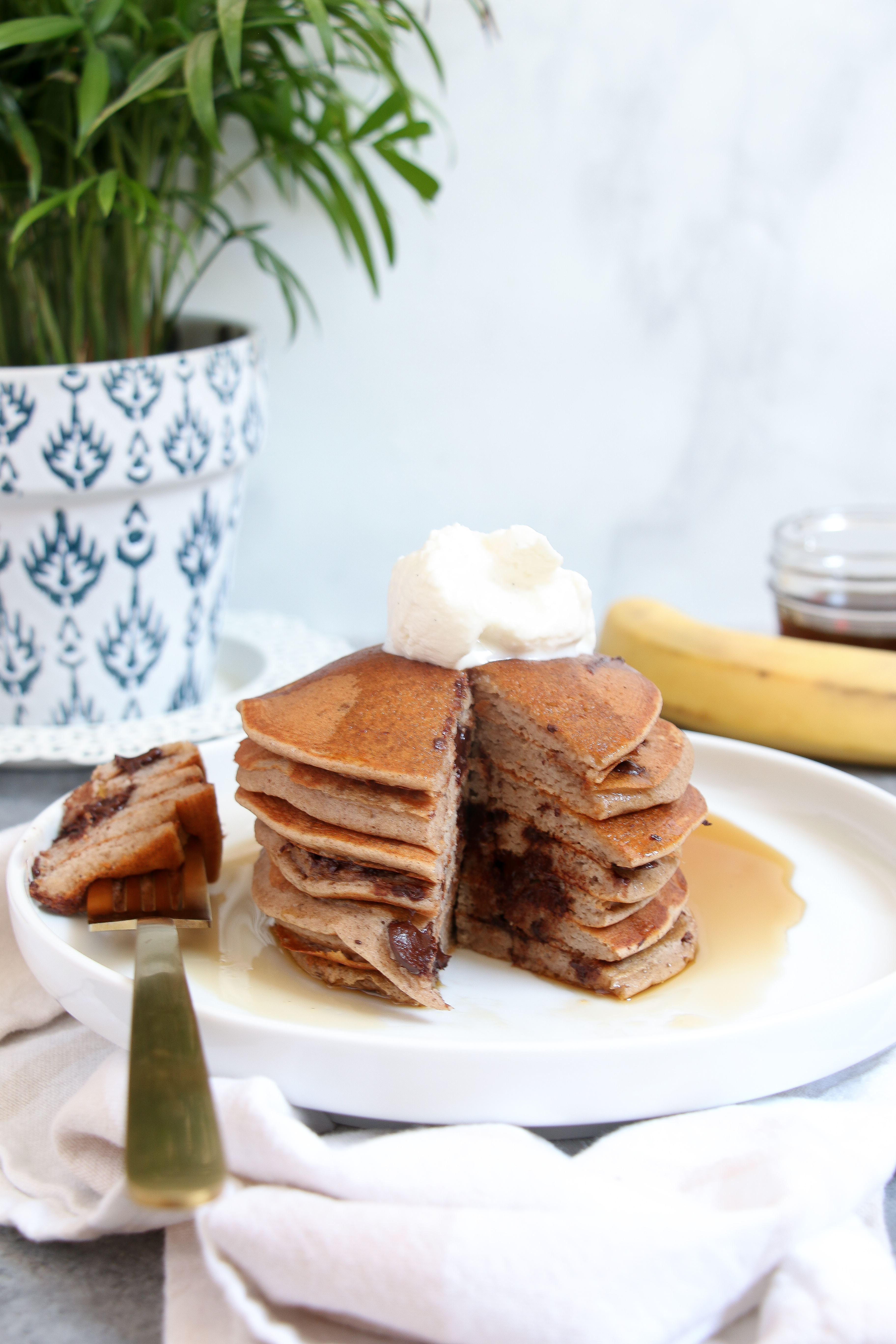 Gluten-free chocolate banana pancakes, topped with Greek yogurt and maple syrup on a white plate