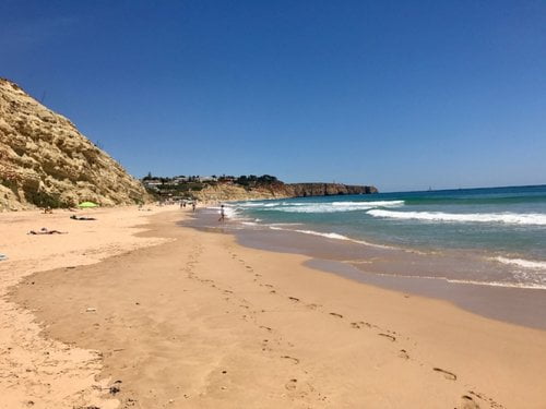 Praia do Porto de Mós beach.: Cliff, yellow sand and blue waves.