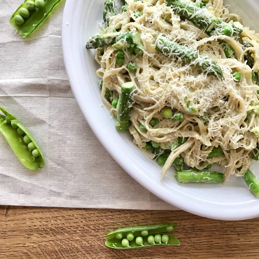 Creamy lemon pasta with asparagus, peas, and mint, on a white plate, on a wooden table.