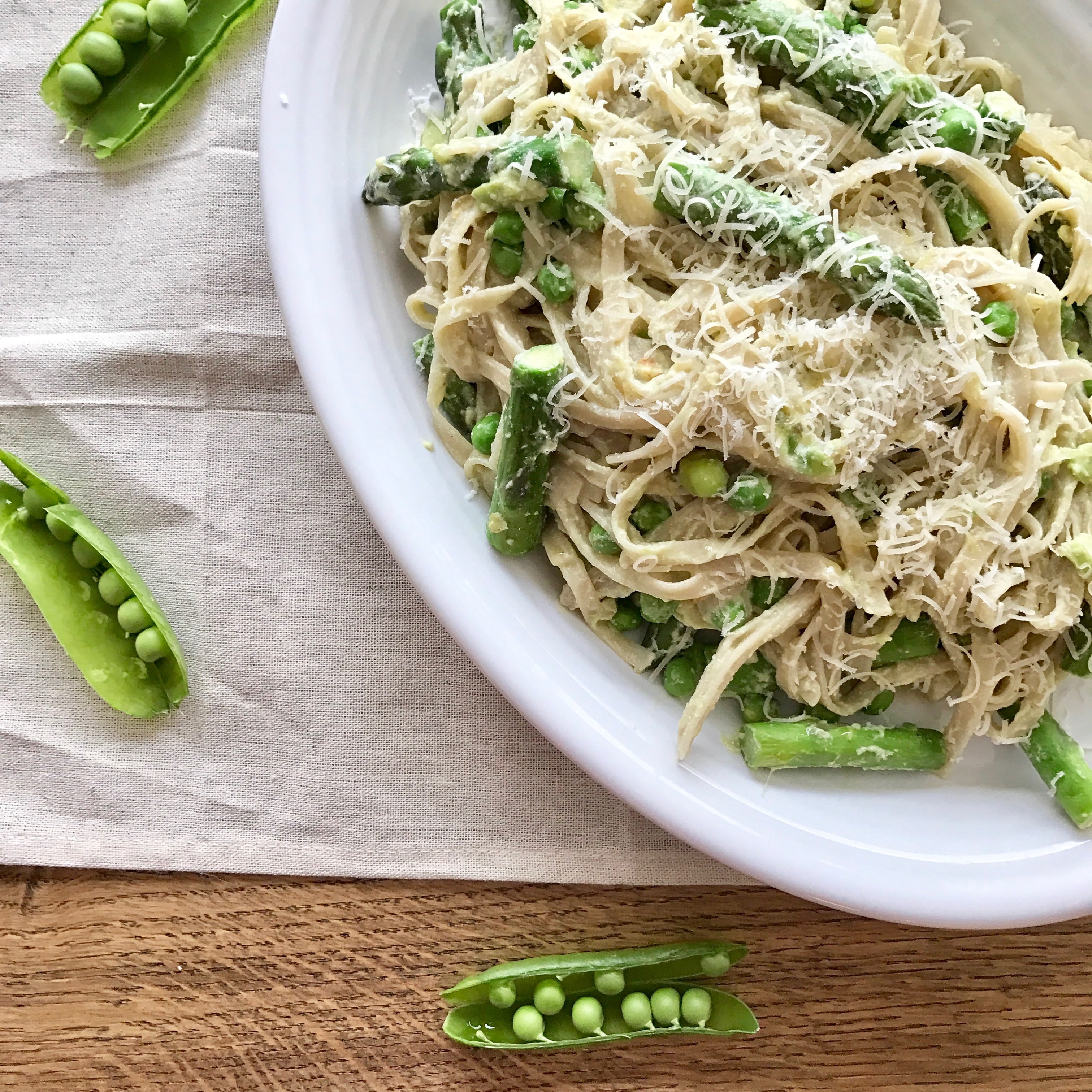 Creamy lemon pasta with asparagus, peas, and mint, on a white plate, on a wooden table.
