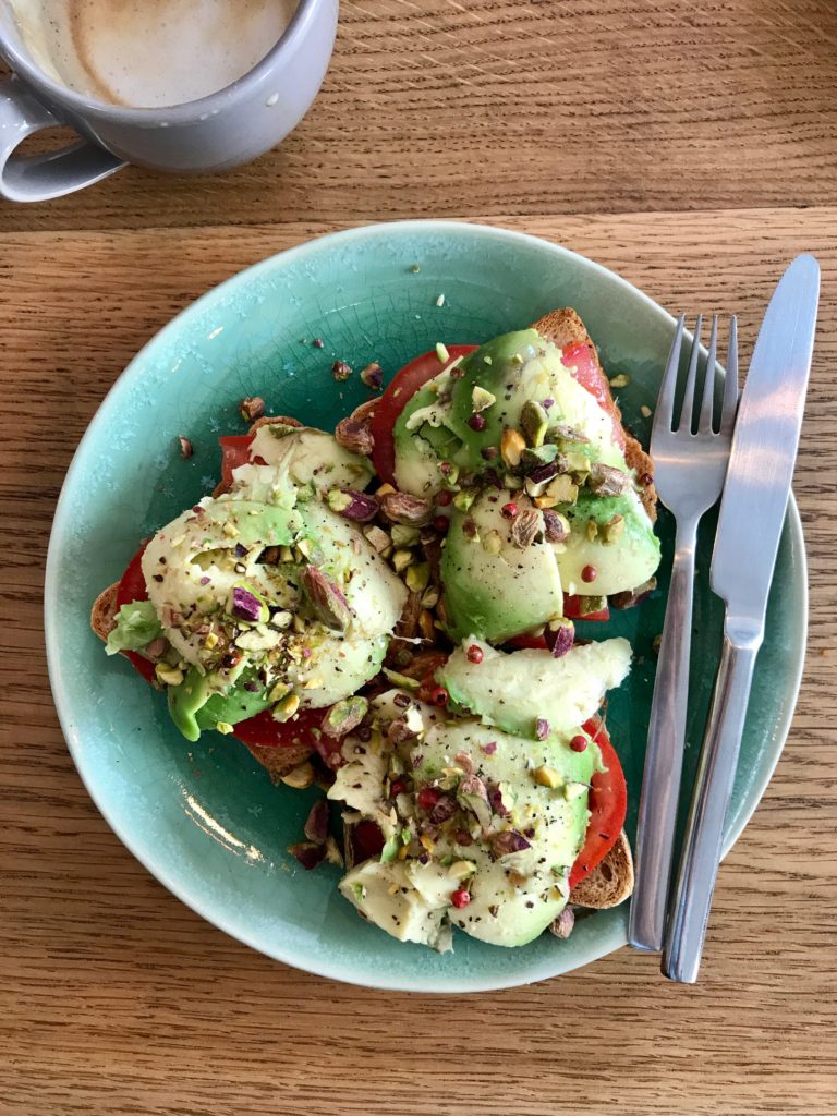 Avocado toast with tomato, crushed pistachios, peppercorns and salt, on a blue plate, on a walnut background.