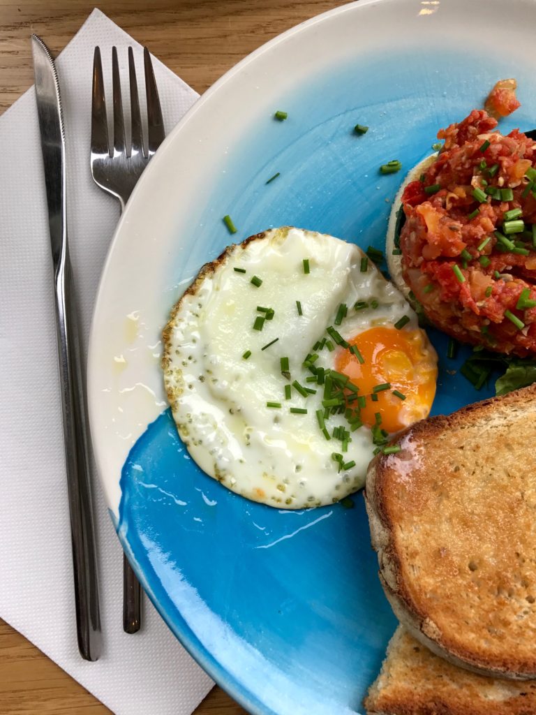 omatoes, chorizo and spinach on top of bread with a fried egg, on a blue plate.