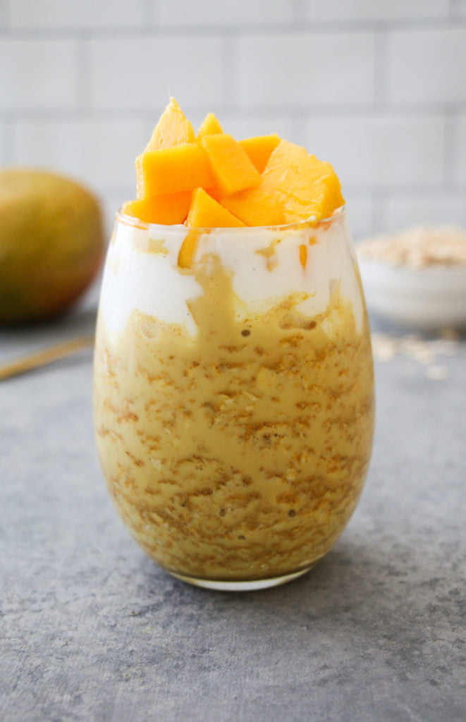 Golden milk overnight oats in a clear glass on a gray background.