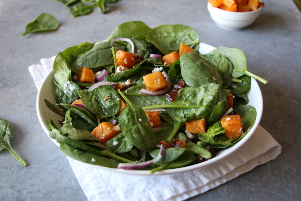 Roasted butternut squash salad in a white bowl, on a white cloth, with a gray background.