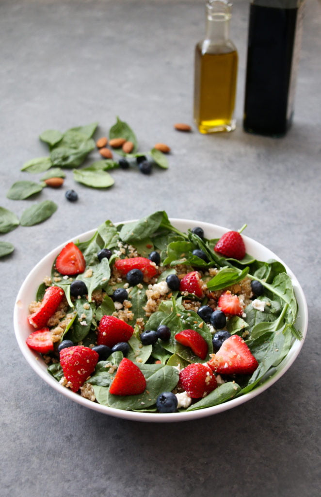 Summer berry and quinoa salad in a white bowl on a gray background.