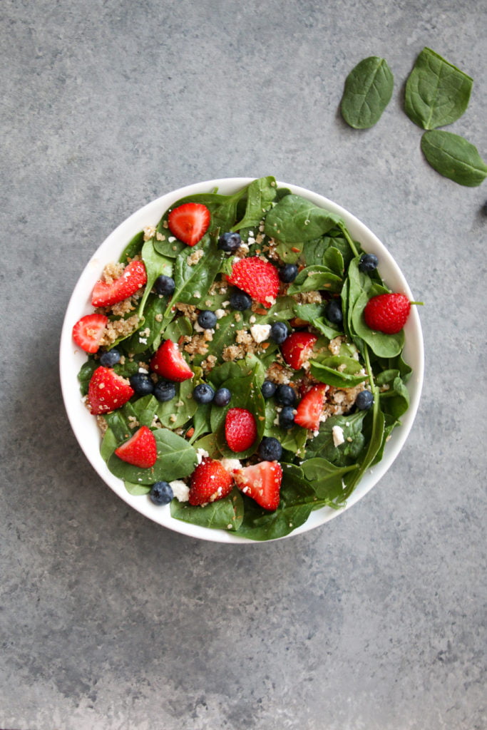 Summer berry and quinoa salad in a white bowl, on a gray backdrop.