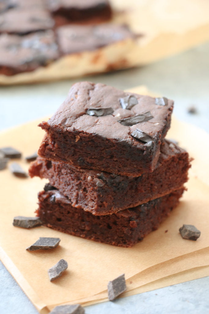 Vertical stack of three chocolate cake bars, surrounded by chocolate chips, on parchment paper.