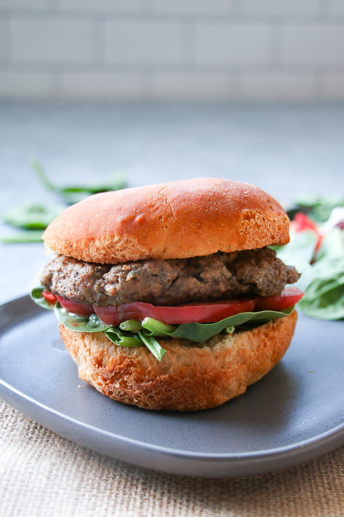 Beef and mushroom burger with lettuce and tomato on a gray plate, with a subway tile backsplash.