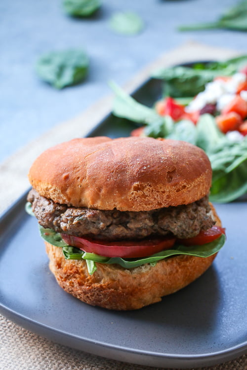 Beef and mushrooms burger with lettuce and tomato, on a gray plate, with salad leaves in the background.