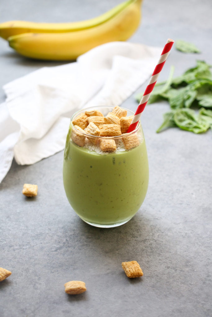 Tropical turmeric green smoothie in a clear glass with a red and white straw, on a gray background.