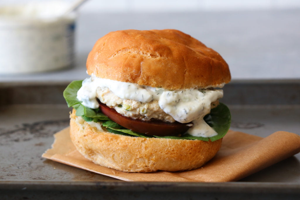 Greek chicken burger on a black tray with tzatziki in the background.