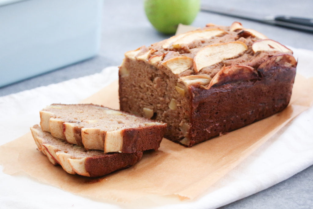 GF apple and cinnamon banana bread slices on parchment paper with a load tin in the background.