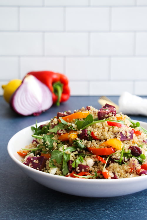 Roasted veggie quinoa salad up-close, in a white bowl, on a navy blue background.