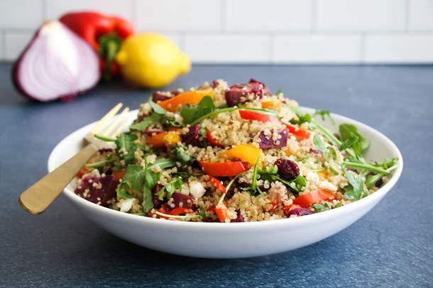 Vegetarian roasted veggie quinoa salad in a white bowl, on a navy blue background.
