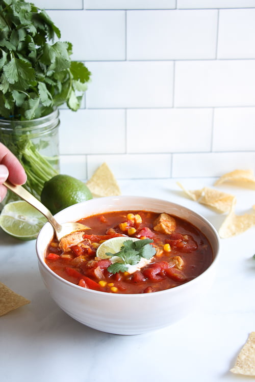 Chicken tortilla soup, topped with Greek yogurt, lime and cilantro, on a marble background.