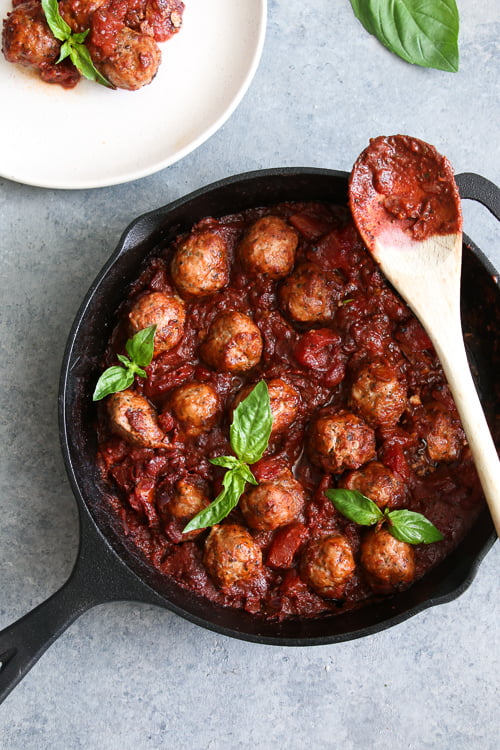 Easy turkey meatballs in spicy tomato sauce, in a black cast-iron pan, on a gray background. 