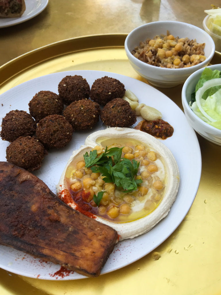 Falafel, hummus and fried eggplant on a white plate, on a gold tray.
