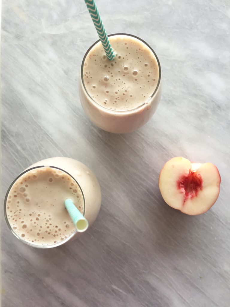 Two peaches and cream smoothies in clear glasses on a marble background.