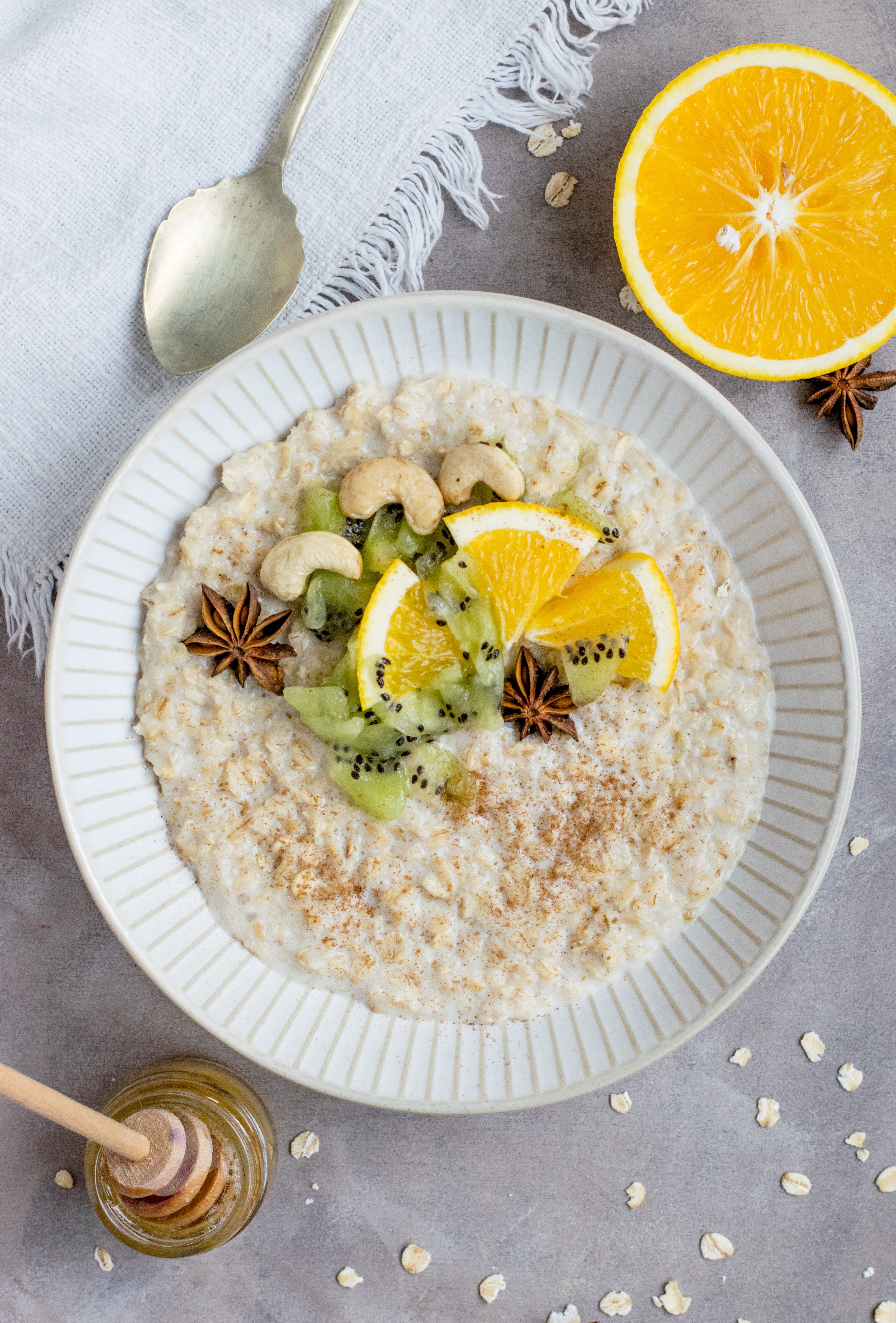 Bowl of oatmeal topped with orange and kiwi on a gray background.