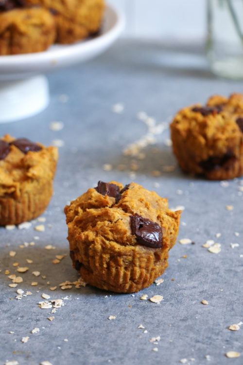 Three pumpkin and chocolate chunk muffins on a gray background, sprinkled with oats
