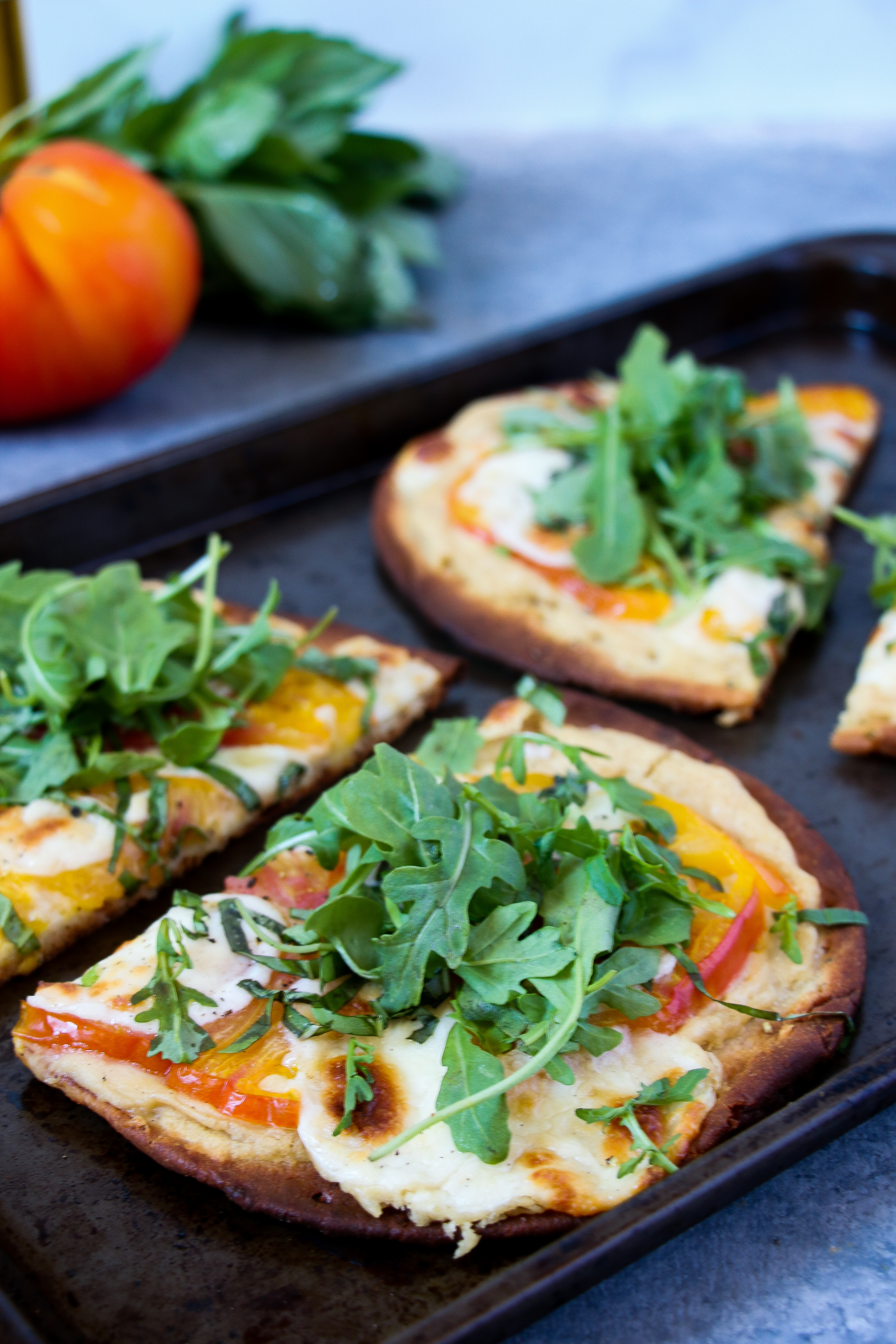 Slice of hummus-margherita pizza on black baking tray on a gray background