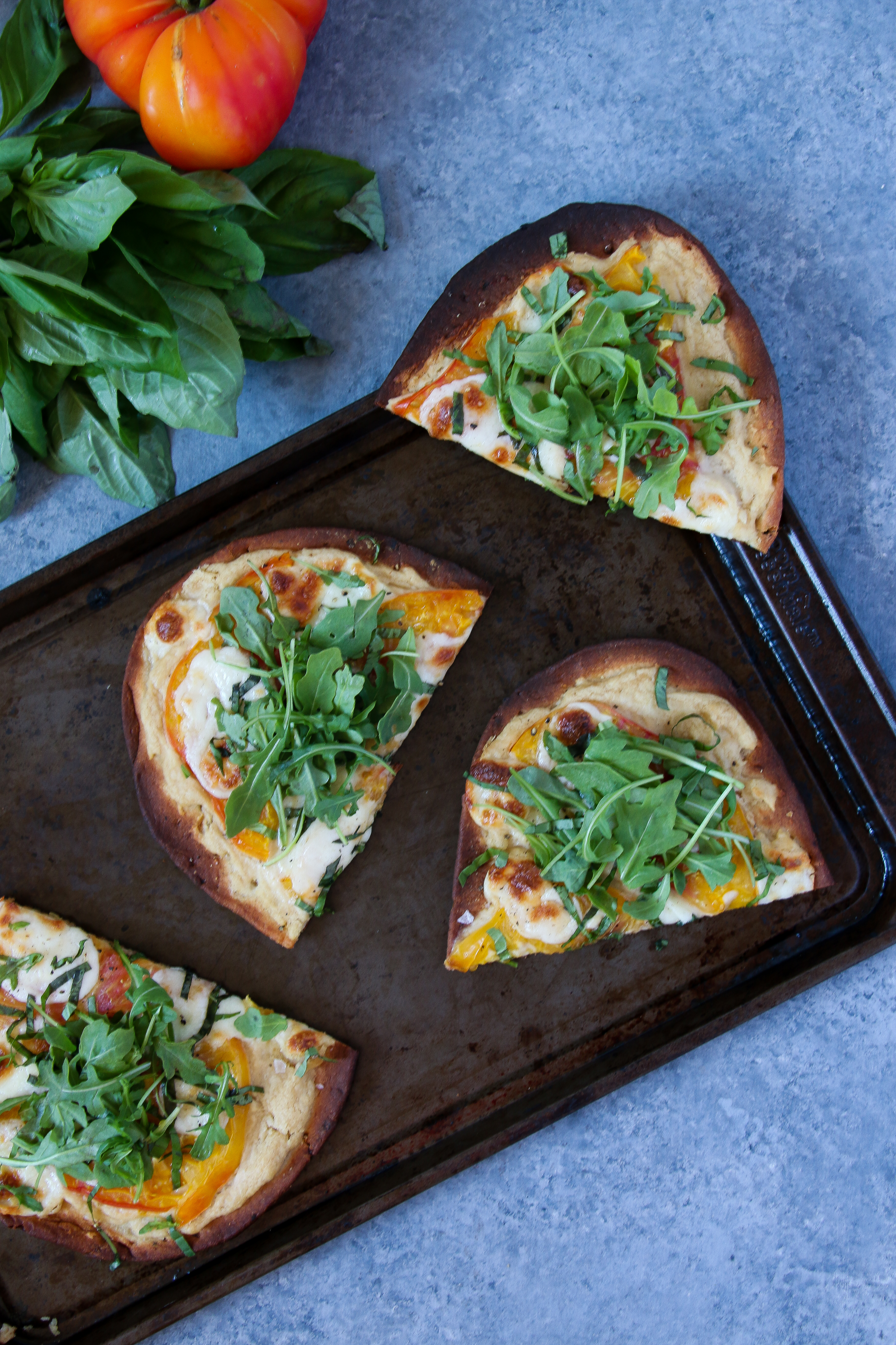 Slices of hummus-margherita pizza on a black baking sheet on a black background