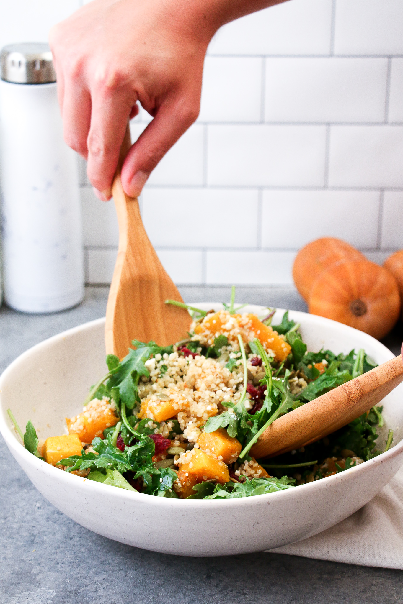 Pumpkin, cranberry and arugula being tossed in a white bowl