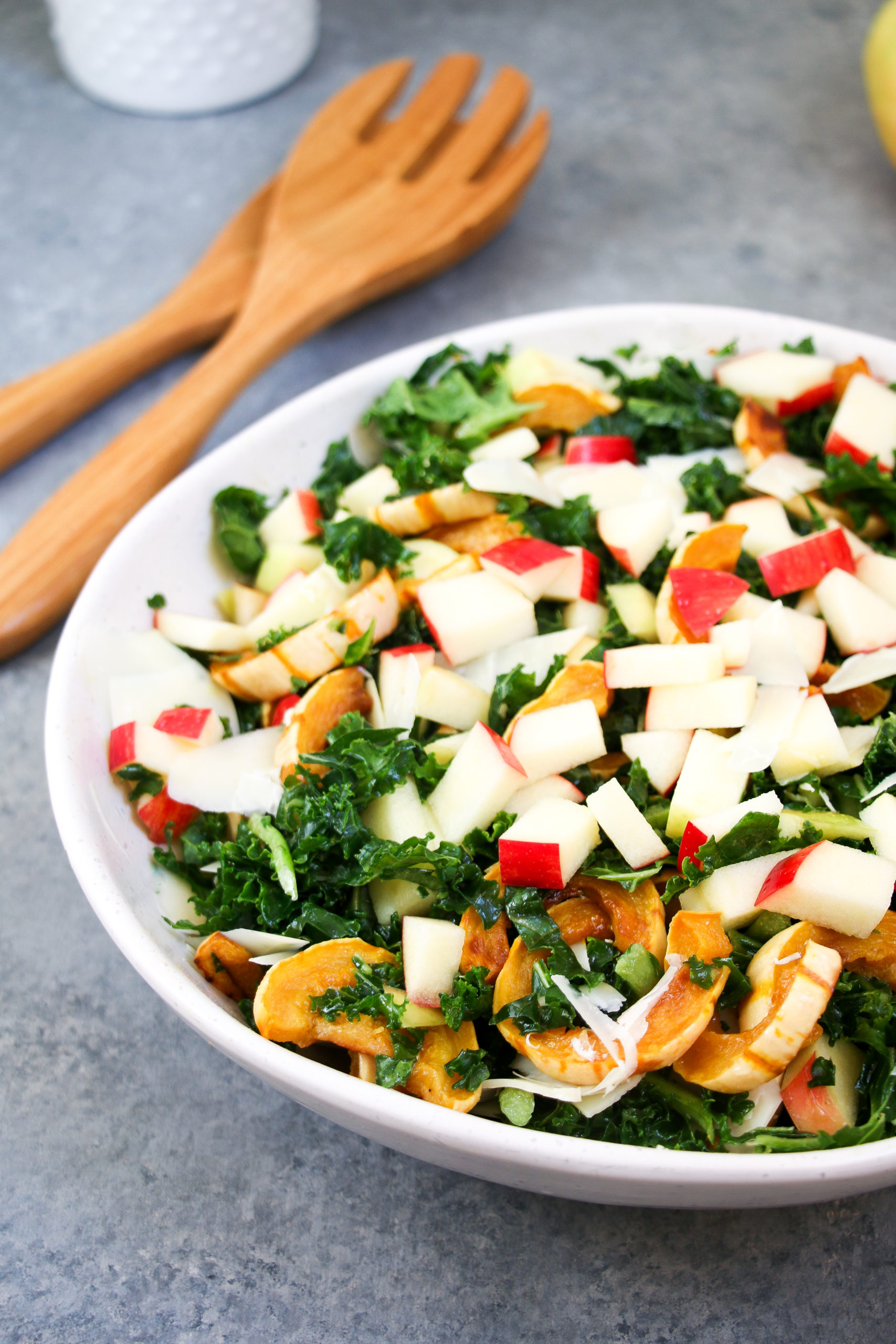Close-up of delicata squash and apple kale salad in a white bowl on a gray background