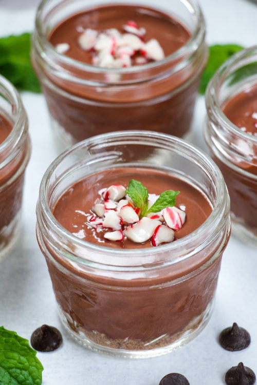 Side on shot of mint-chocolate cheesecake cups, topped with candy canes, on a white background.