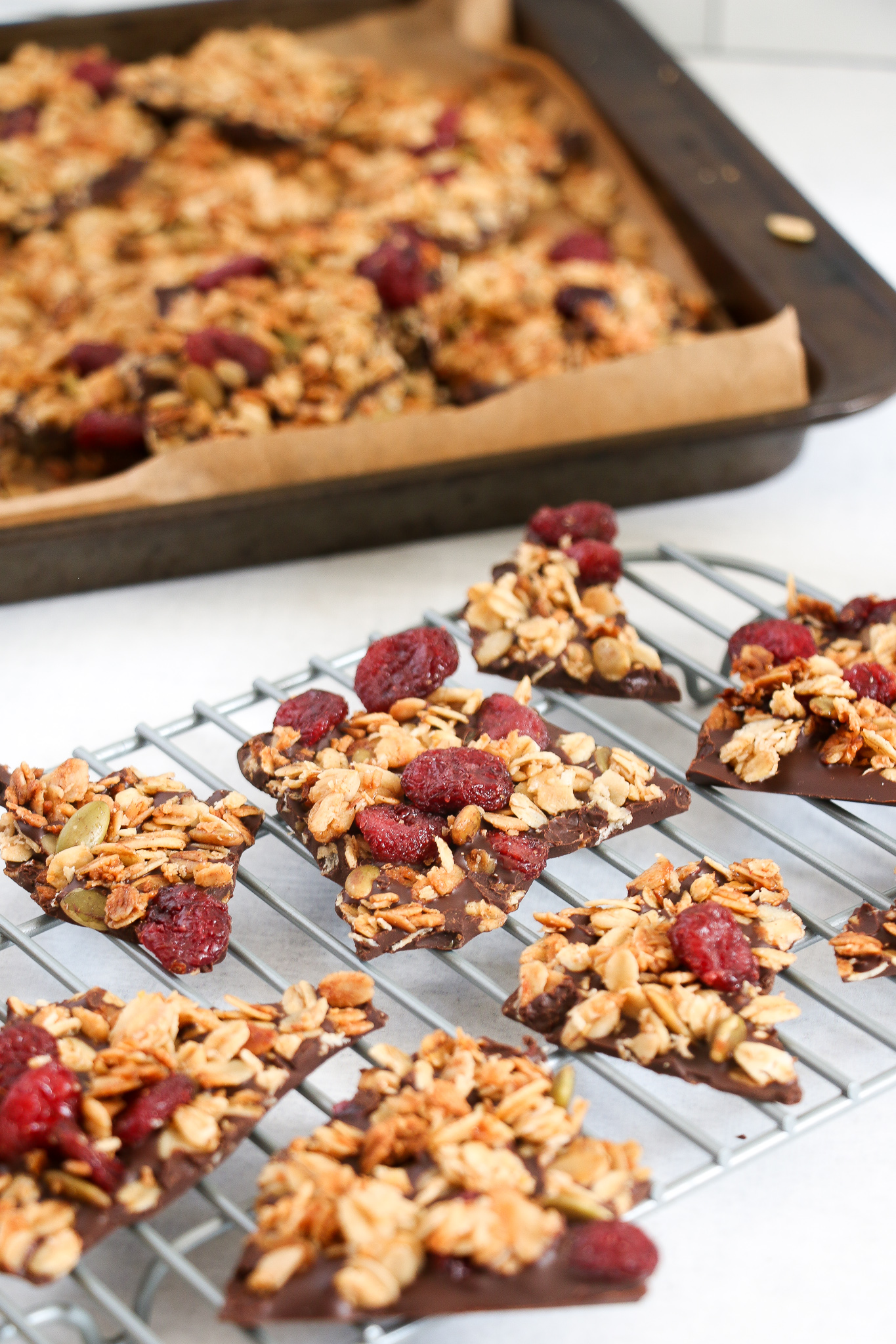 Dark chocolate granola bark pieces on a cooling rack on a white background.