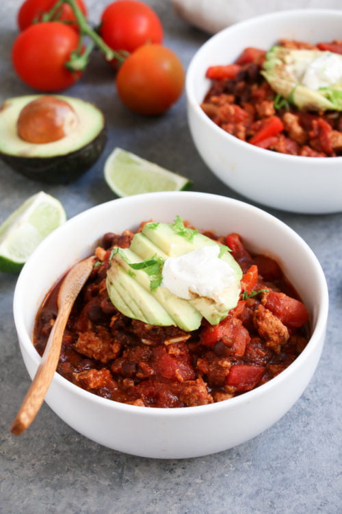 Close up of turkey-black bean chili in a while bowl on a gray background.