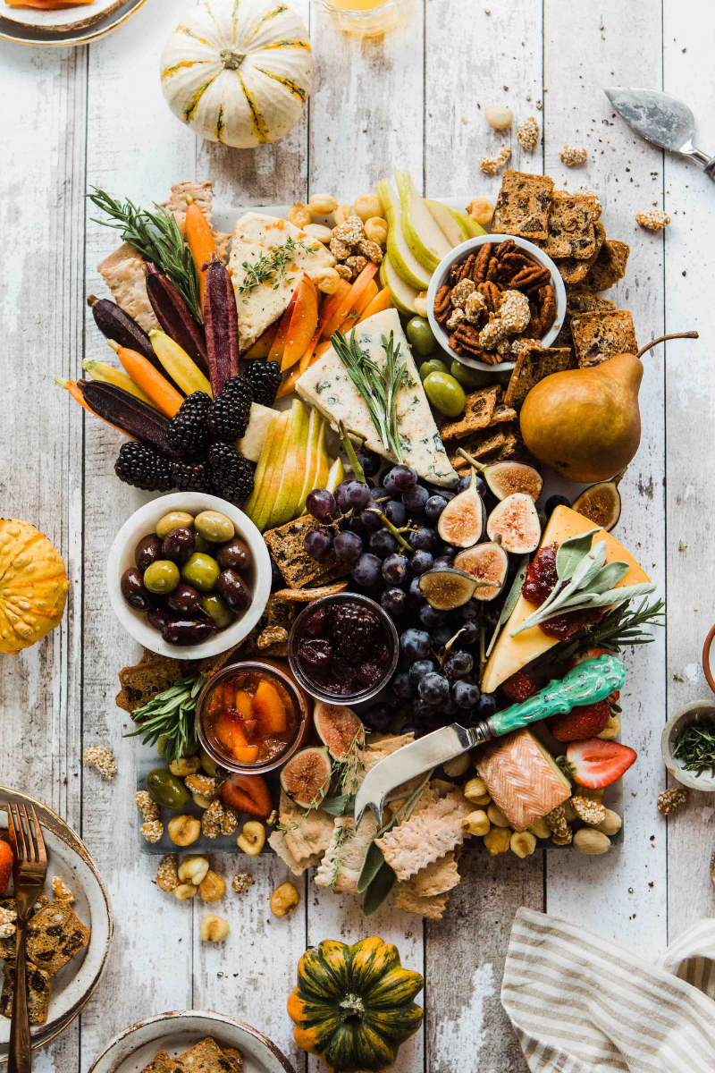 Healthy cheese board with cheese, fruit, veggies, nuts, and wholegrain crackers, on a white background