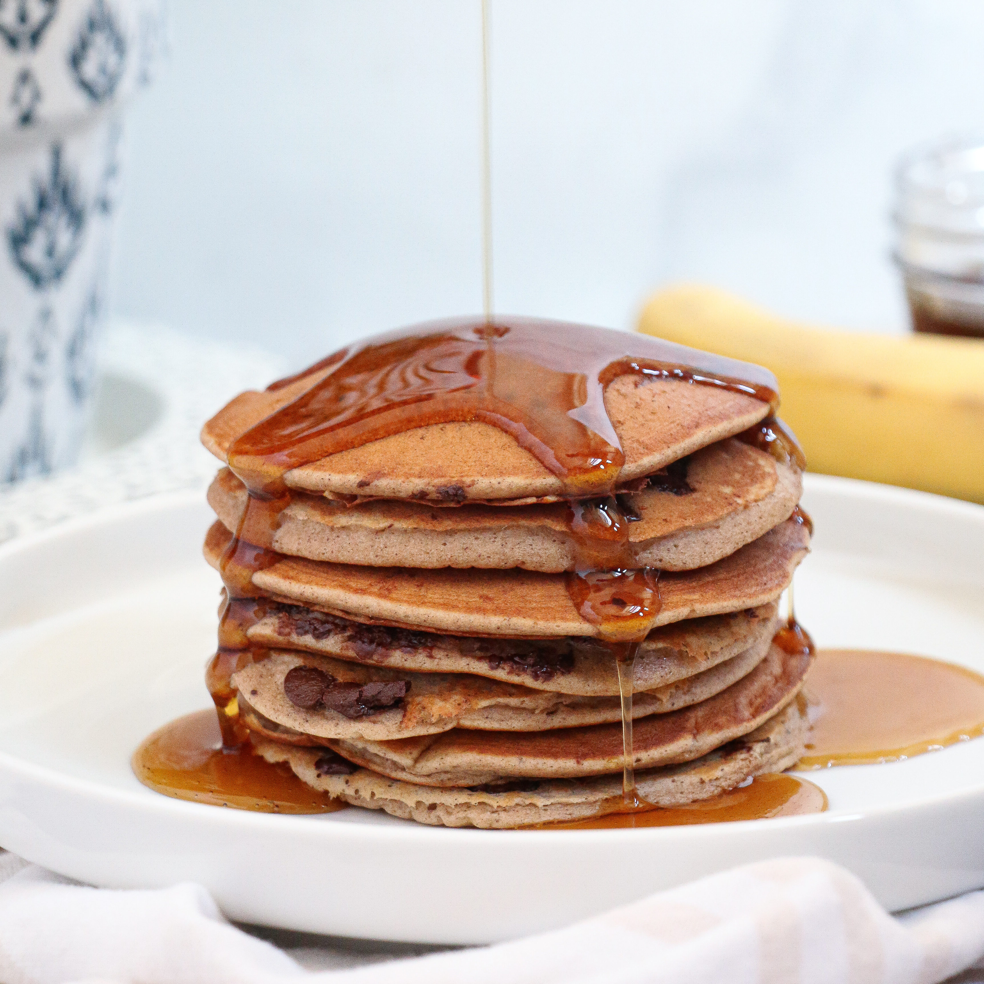 Chocolate chip banana pancakes drizzled with maple syrup on a white plate