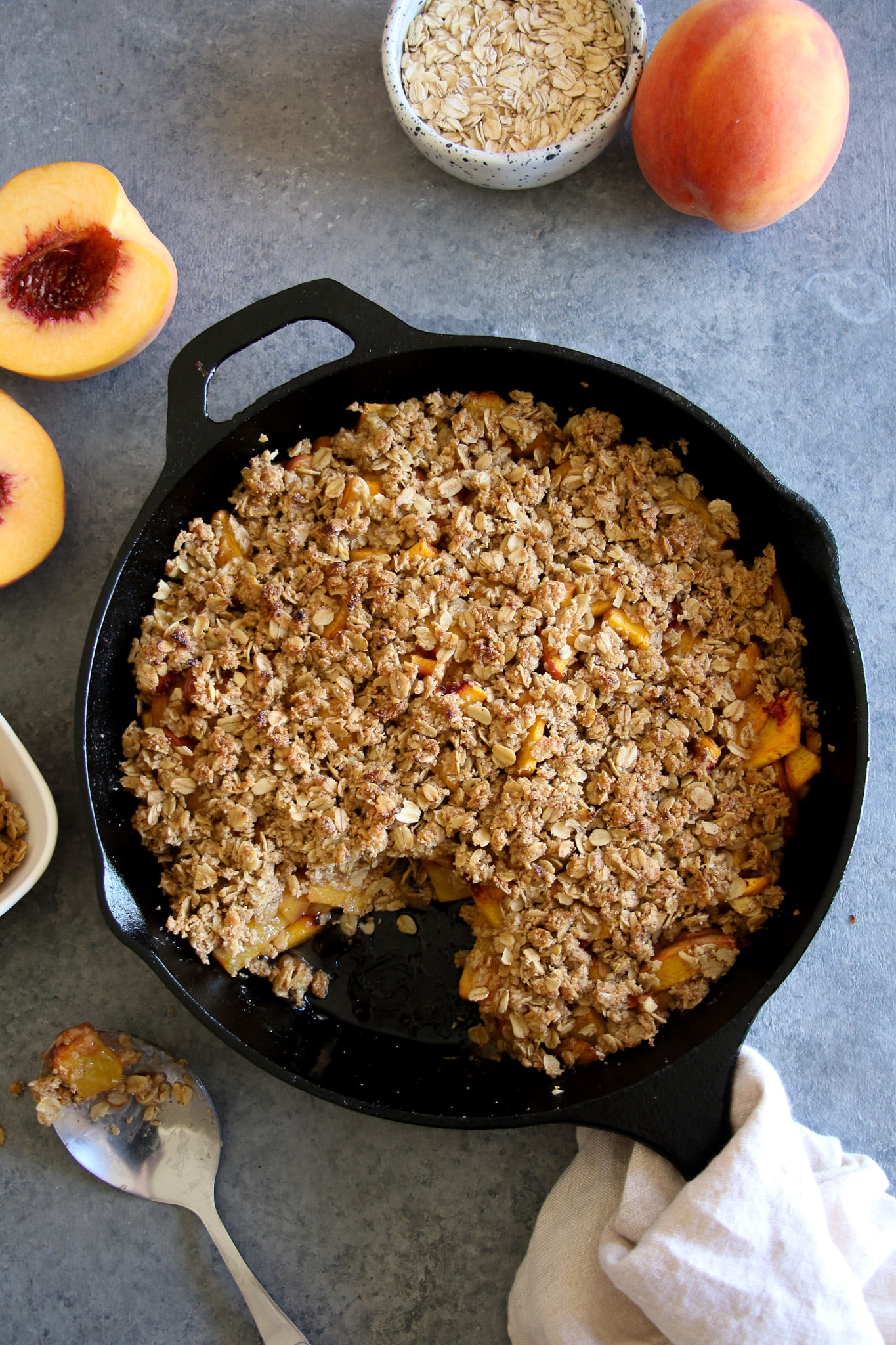 gluten-free peach crisp with a scoop removed in a cast iron pan on a gray background